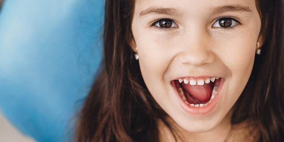 Happy caucasian girl with opened mouth smiling at camera after a teeth examination at the pediatric dentist