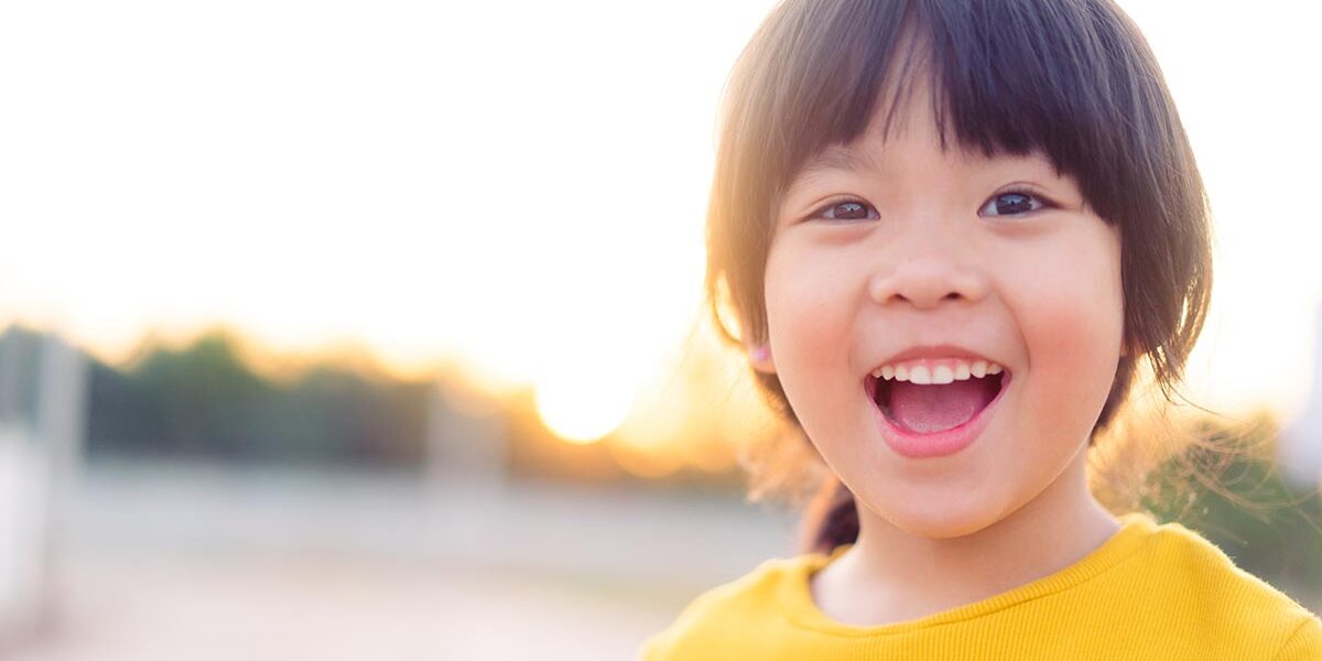 A girl smiling outside smiles at the camera.